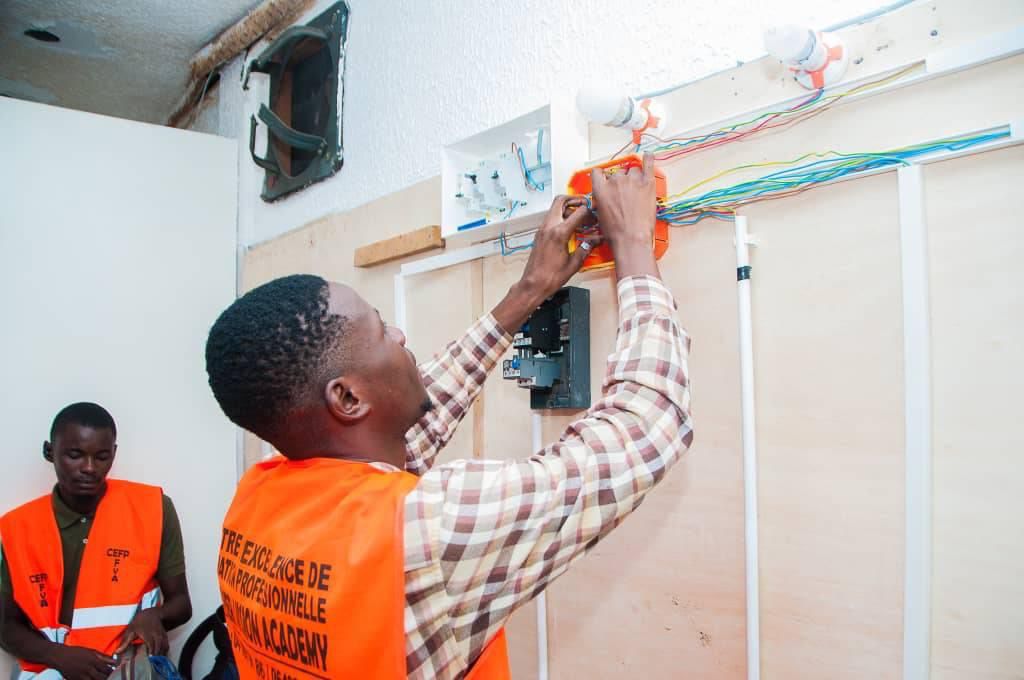 Apprenants en gilet FVA installant un tableau électrique